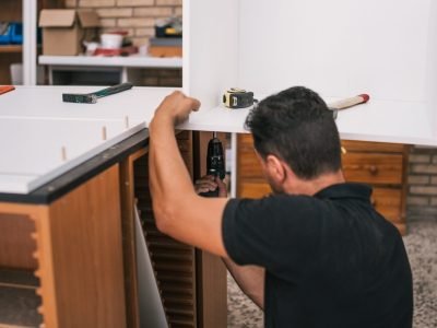 Worker using a drill to build a kitchen furniture Worker using a drill to put together two perpendicular pieces of kitchen furniture in a workshop